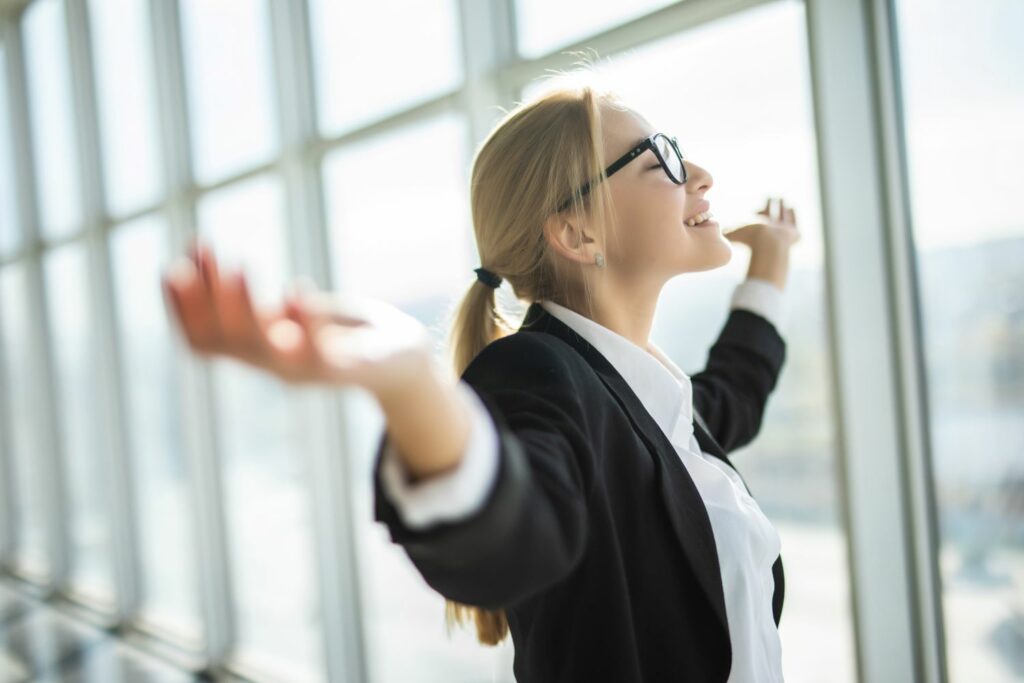 femme les bras en croix dans un bureau souriante car elle a trouver sa voie qui la passionne suite a ses différentes expériences de vie