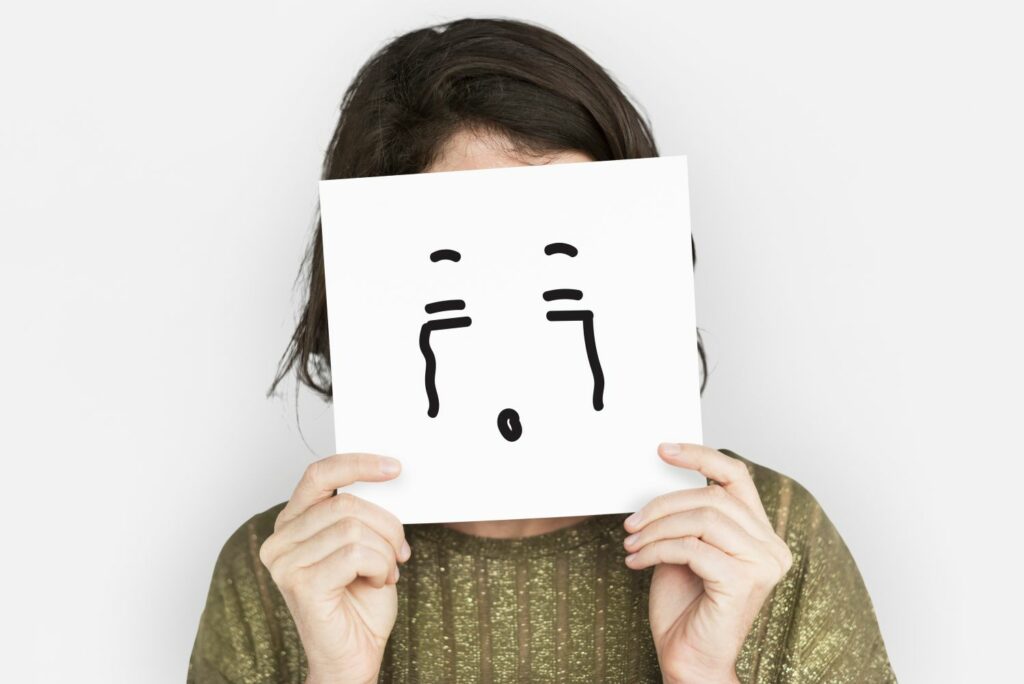 femme qui porte une pancarte avec un visage différent de sa véritable humeur mettant en valeur le fait de refoulé ses émotions