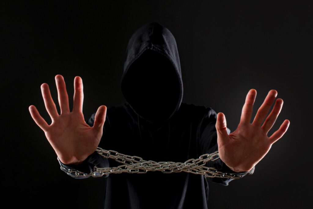 personne en capuche noir sur fond noir main en premier plan avec chaînes montrant il est possible de couper les liens transgénérationnels