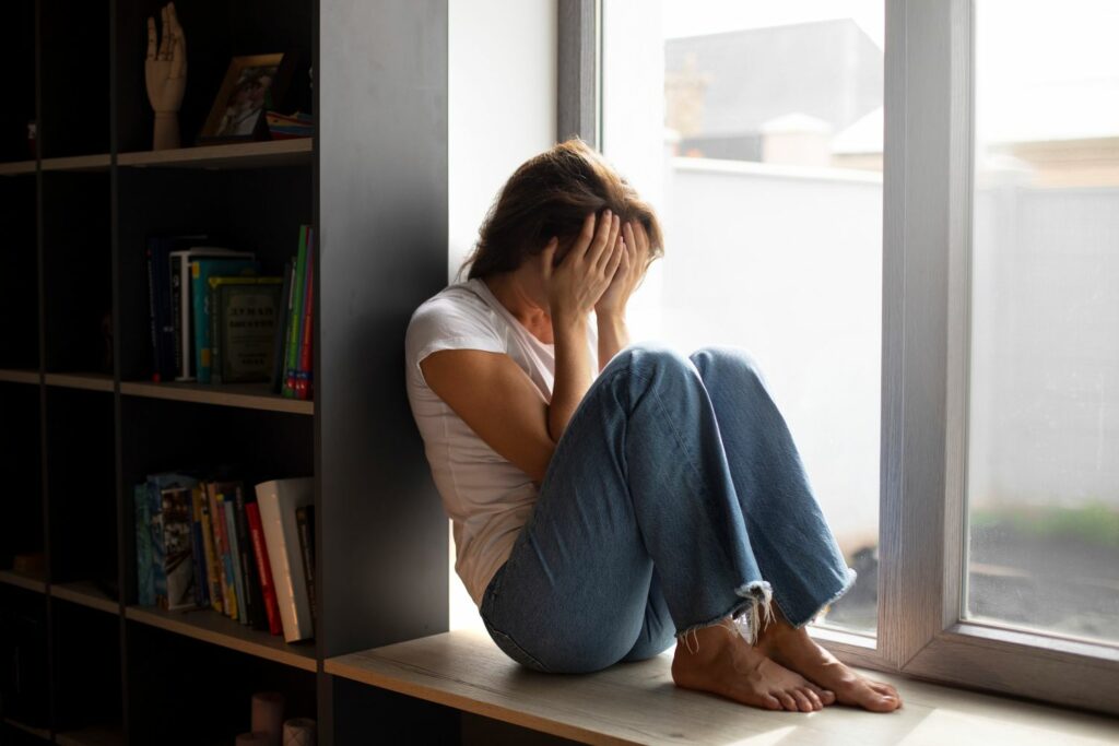 femme triste au bord de la fenêtre montrant Comment les traumatismes se transmettent à travers les générations