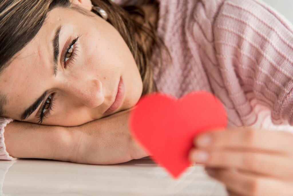 jeune femme regardant un cœur , elle est pensive montrant le caractère en dépendance affective d'avoir du mal a se détacher